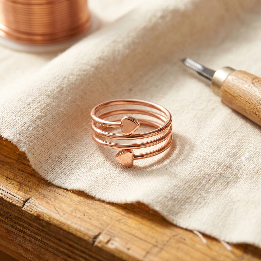 Copper spiral ring with heart detail resting on natural linen fabric beside jewellery-making tools