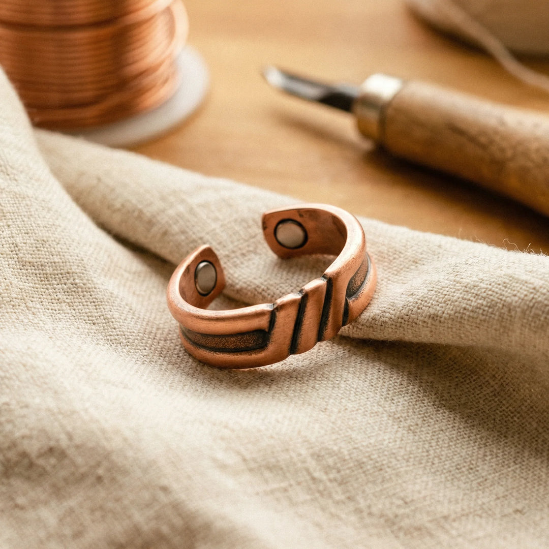 Women's copper adjustable ring with diagonal grooves and magnetic inserts resting on neutral linen fabric