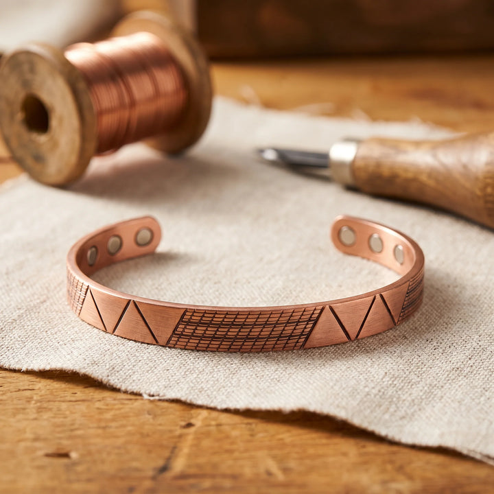 Women's copper cuff bracelet with geometric engraved pattern displayed on neutral linen fabric