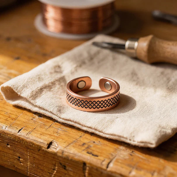 Women's copper ring with hand-engraved lattice pattern resting on linen fabric beside copper wire spool