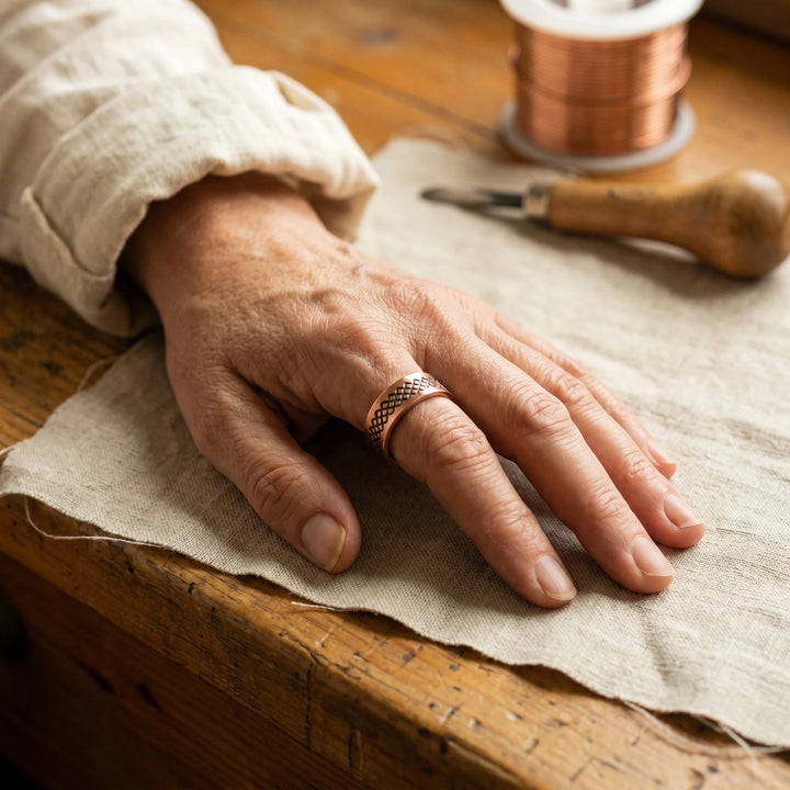 Close-up view of adjustable copper ring showing geometric lattice engraving and open-back band design