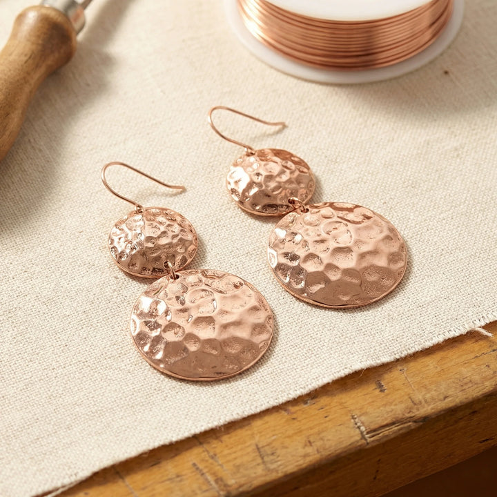 Women's hammered copper drop earrings with double disc design and rose gold finish on neutral background