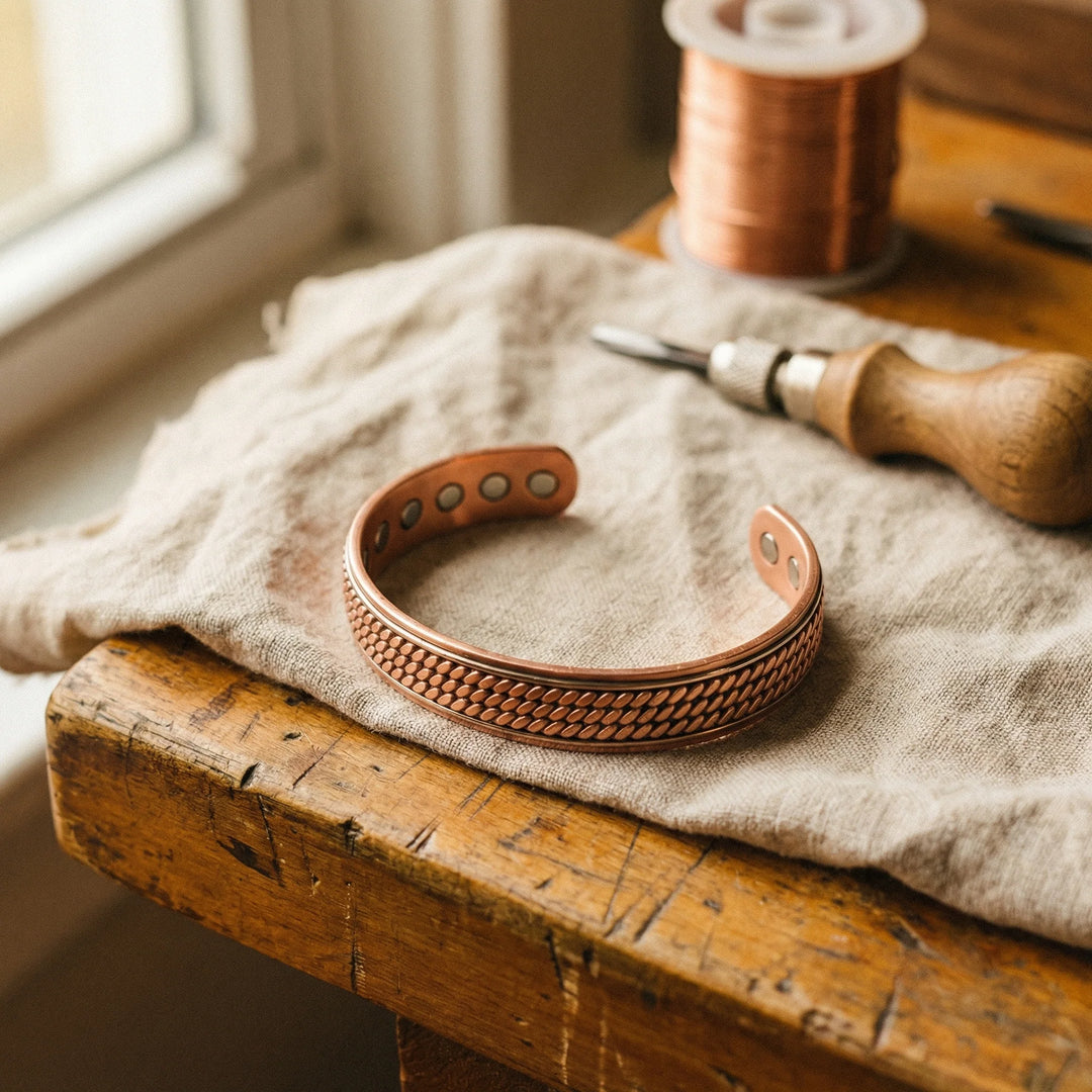 Women's copper cuff bracelet with textured rope pattern resting on linen fabric beside wooden ruler