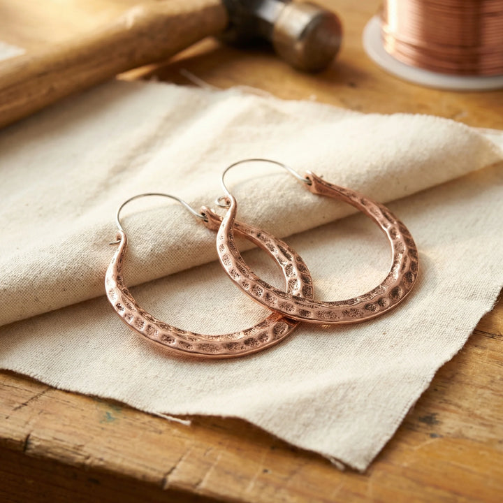 Eden hammered copper hoop earrings in rose copper finish resting on natural linen fabric
