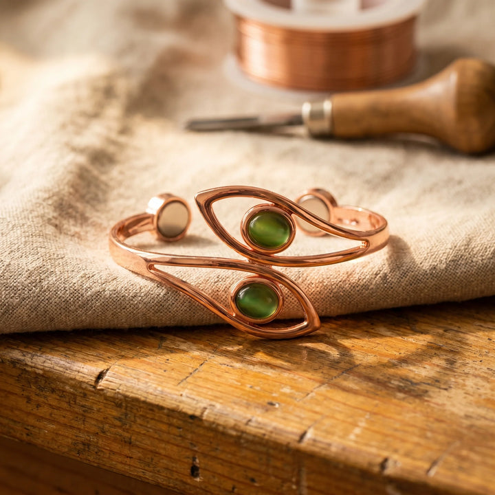Copper cuff bracelet with green stone accents displayed on wooden surface with crafting tools