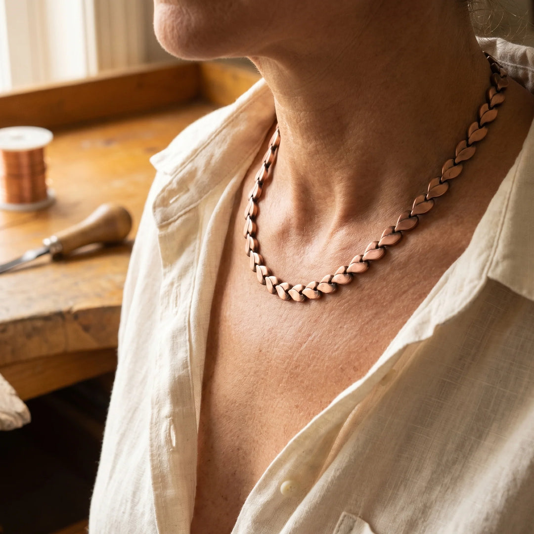 Braided copper necklace with heart-shaped links worn close to the neckline against natural linen top