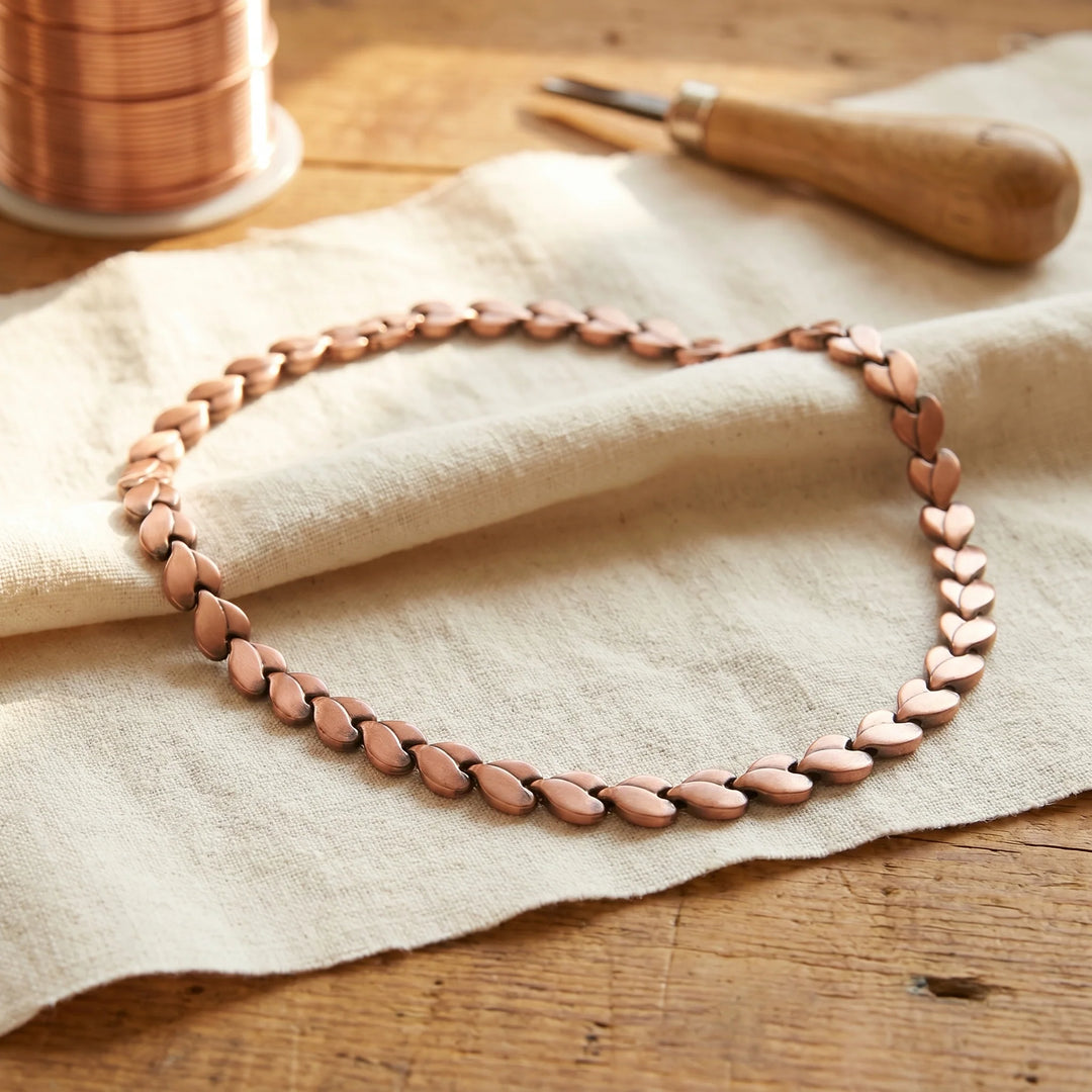 Close-up of handcrafted braided copper chain showing interwoven heart link pattern and warm metal tone
