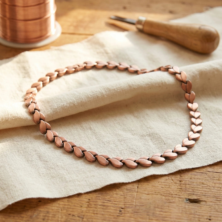 Close-up of handcrafted braided copper chain showing interwoven heart link pattern and warm metal tone