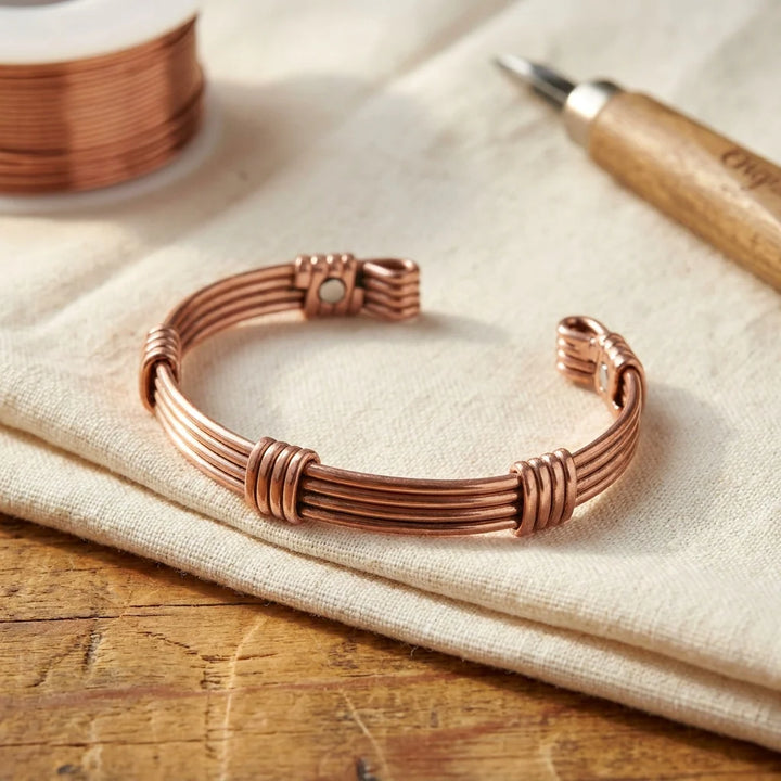 Women's copper cuff bracelet with wire-wrapped ridges displayed on neutral linen surface