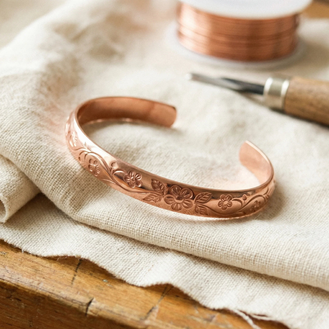 Women's copper cuff bracelet with hand-engraved floral motif resting on linen fabric