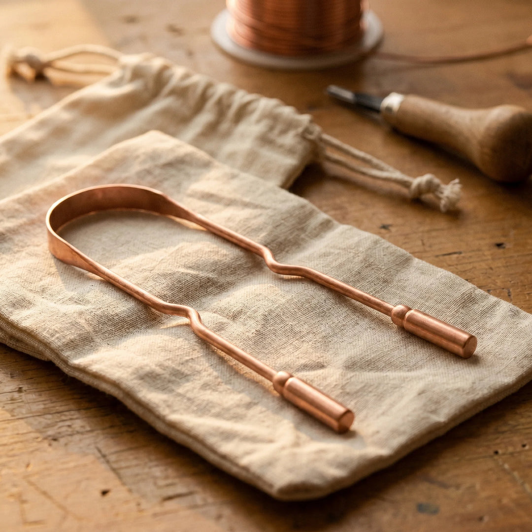 Copper tongue scraper with U-shaped design and rounded handles resting on natural linen fabric on wooden surface