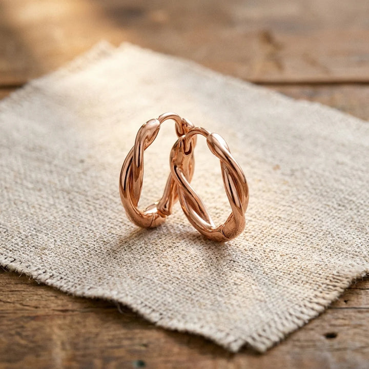 Twisted hoop earrings with spiral design and warm copper-tone finish resting on fabric