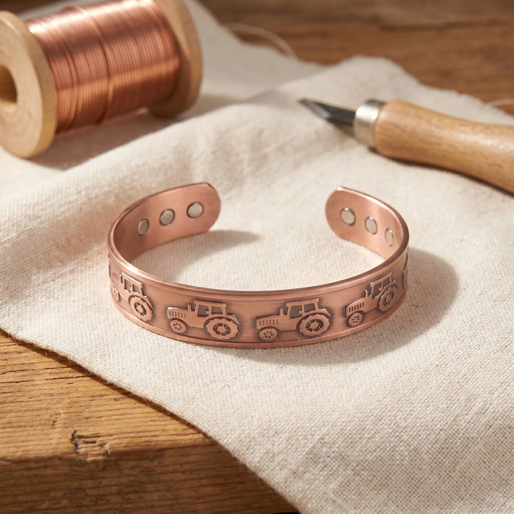 Copper cuff bracelet with embossed tractor motif and magnetic closure on linen fabric