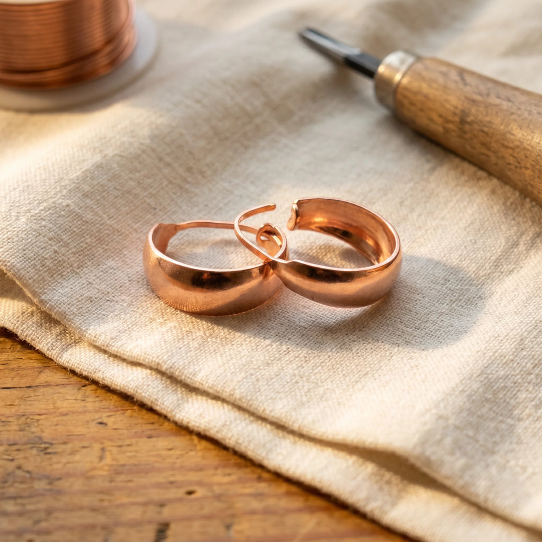 Rose gold hoop earrings with polished finish resting on neutral linen fabric beside crafting tools