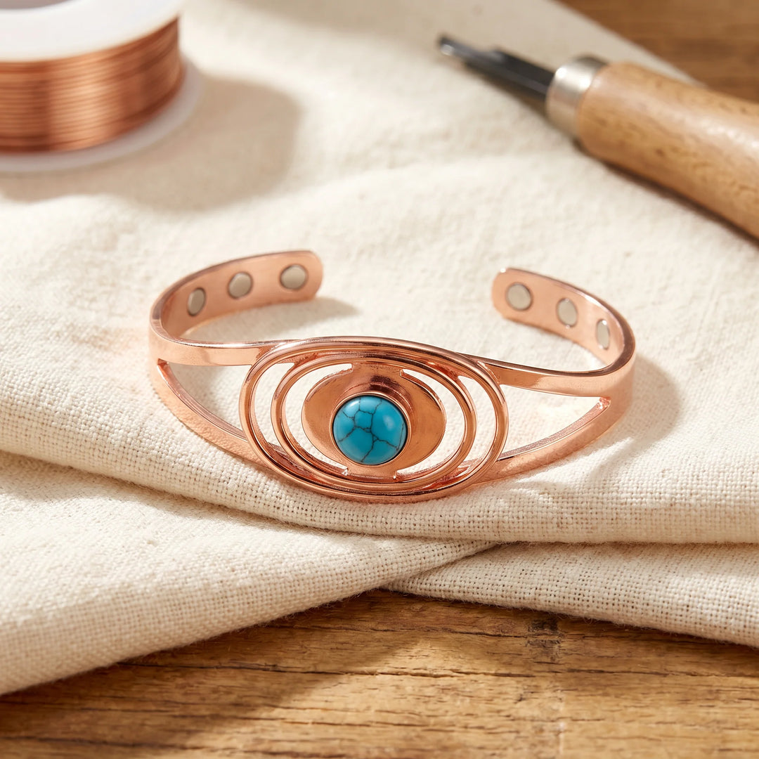 Copper cuff bracelet with concentric oval design and turquoise stone centrepiece displayed on neutral linen fabric