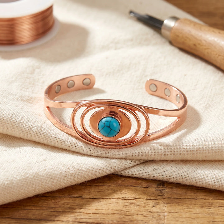 Copper cuff bracelet with concentric oval design and turquoise stone centrepiece displayed on neutral linen fabric