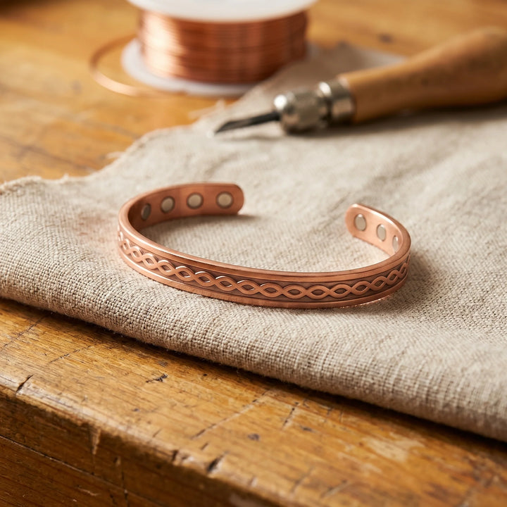Women's copper cuff bracelet with engraved infinity pattern and magnetic closure on linen fabric