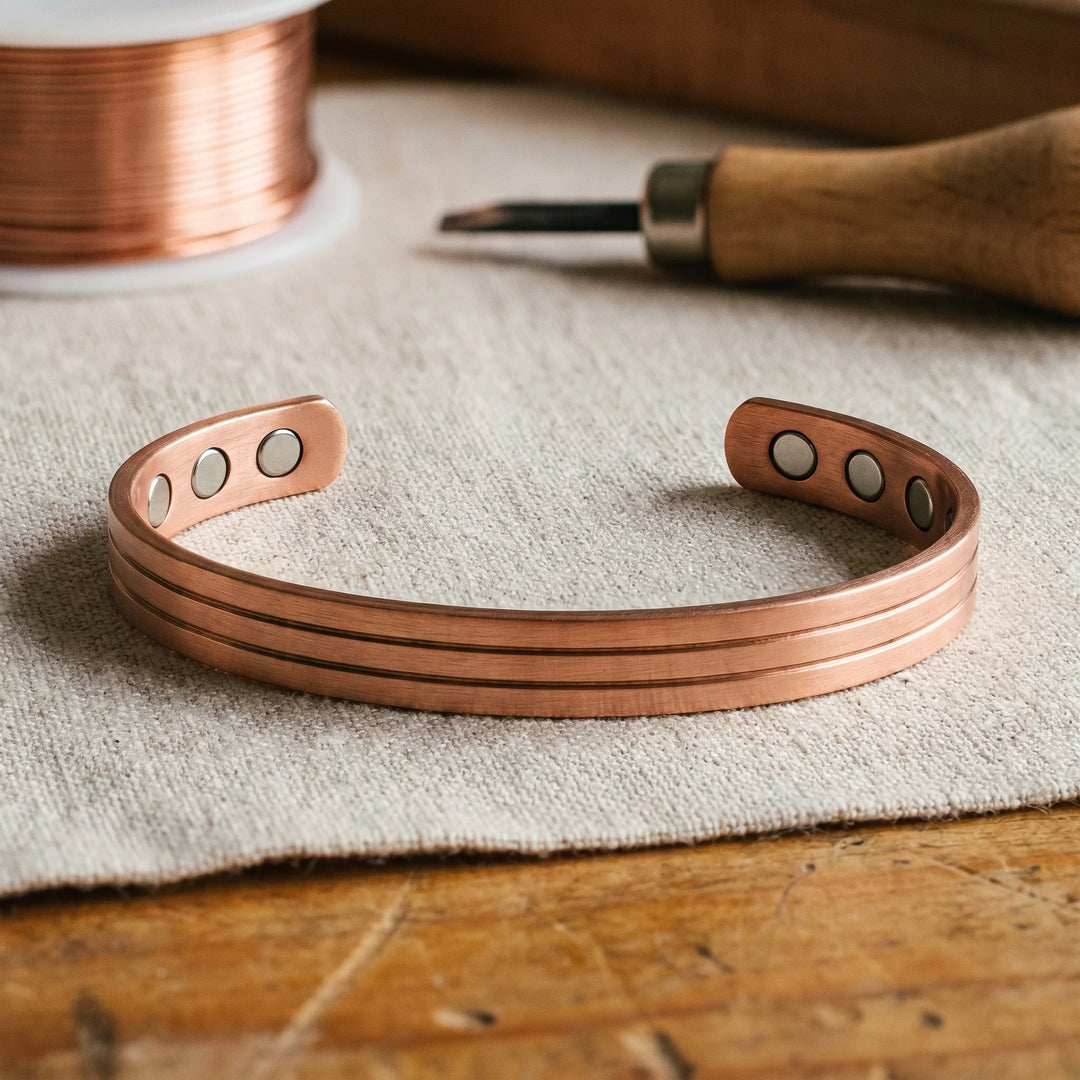 Women's copper cuff bracelet with three grooved channels displayed on neutral fabric surface