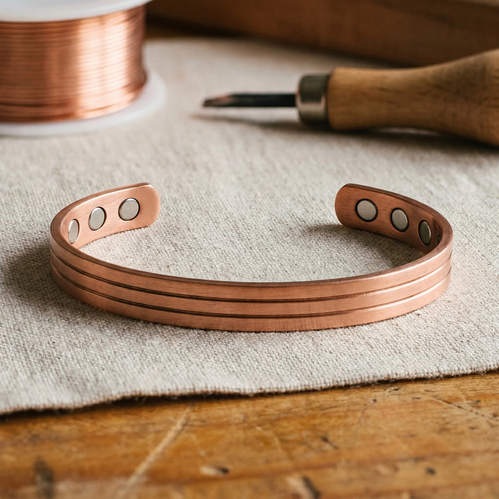 Women's copper cuff bracelet with three grooved channels displayed on neutral fabric surface