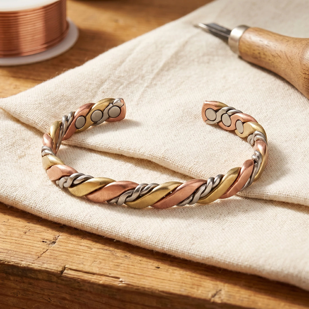 Women's twisted copper bangle with tri-tone braided design resting on linen fabric beside copper wire