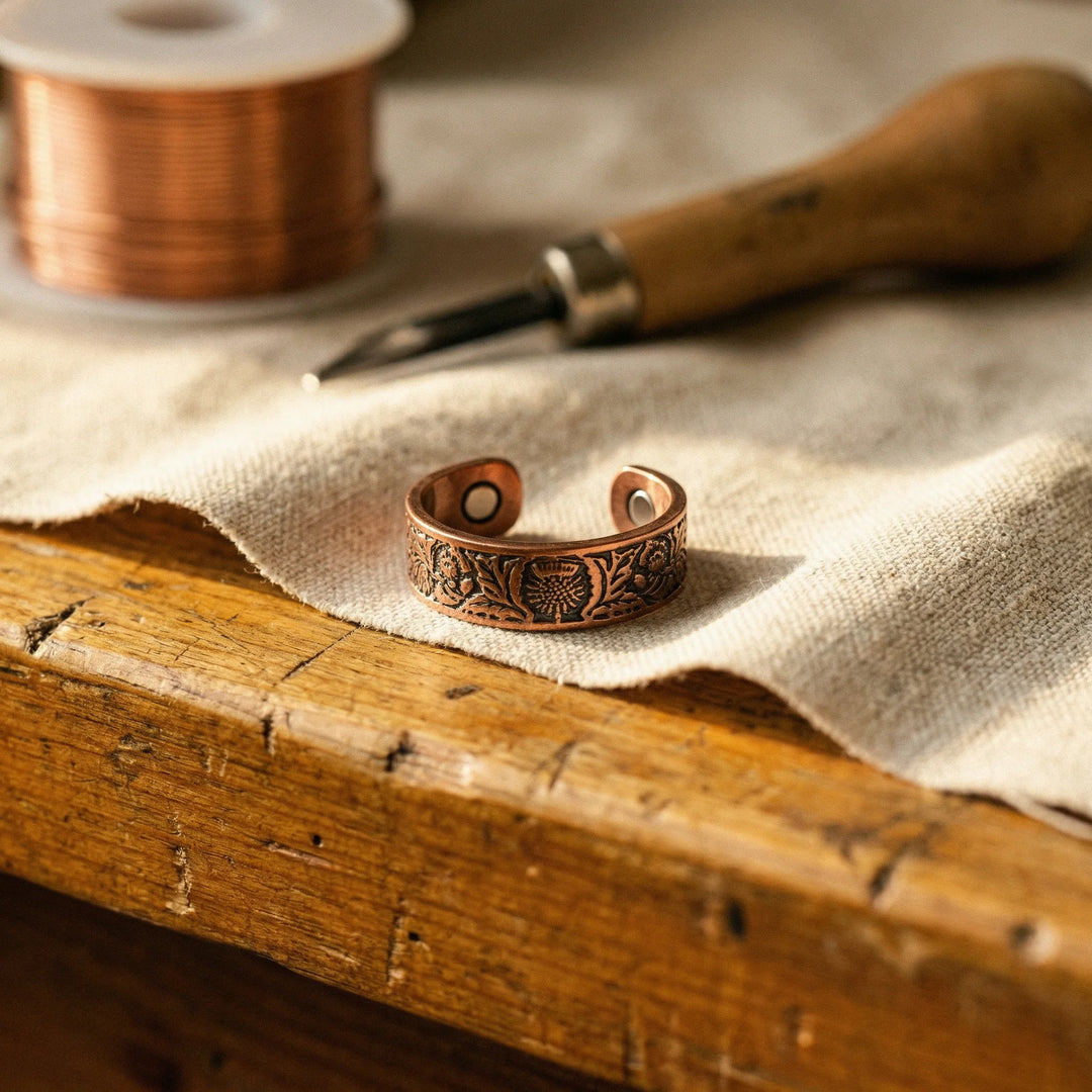 Copper cuff ring with embossed floral detailing resting on linen fabric beside crafting tools