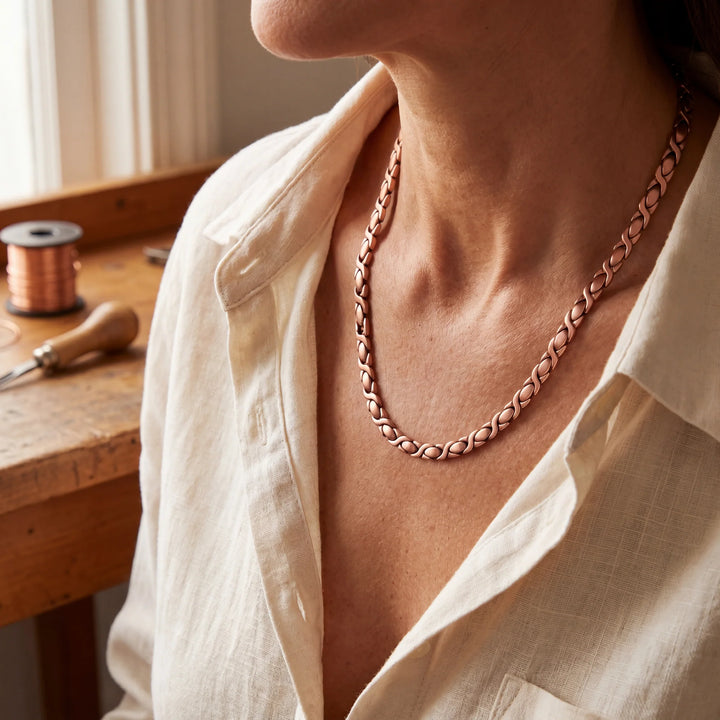 Copper chain necklace with interlocking X-links resting at the collarbone over a white linen blouse