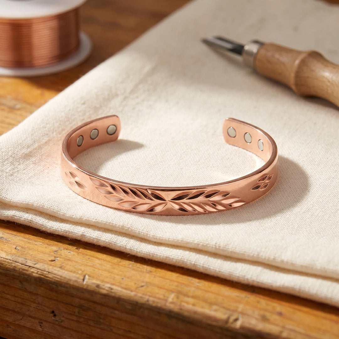 Copper cuff bracelet with hand-engraved leaf pattern resting on neutral linen fabric