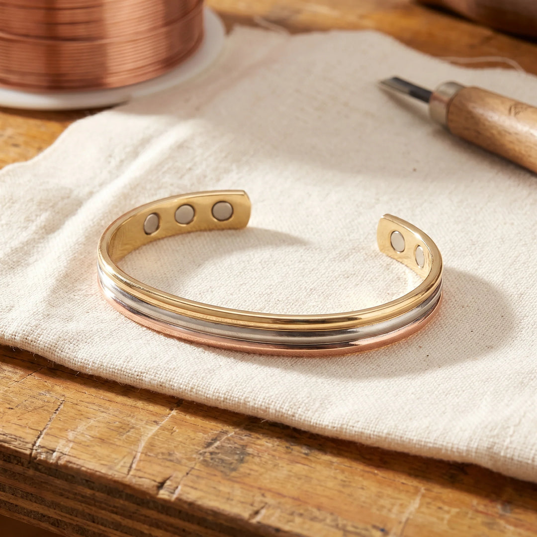 Tri-tone copper magnetic cuff bracelet with rose gold silver and gold bands on linen cloth