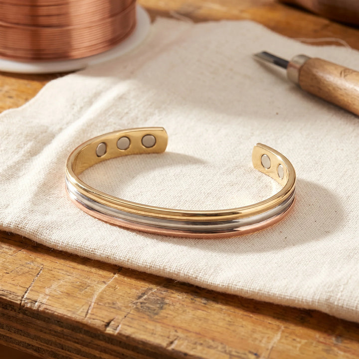 Tri-tone copper magnetic cuff bracelet with rose gold silver and gold bands on linen cloth