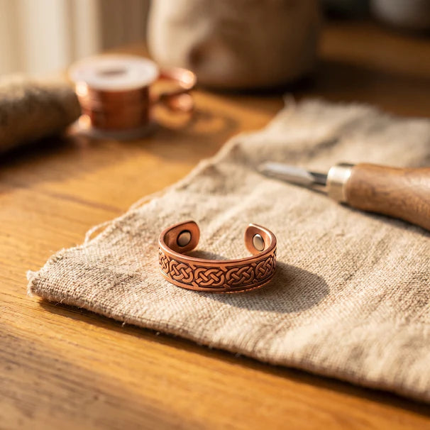 Copper magnetic ring with Celtic knotwork pattern displayed on neutral linen fabric with crafting tools