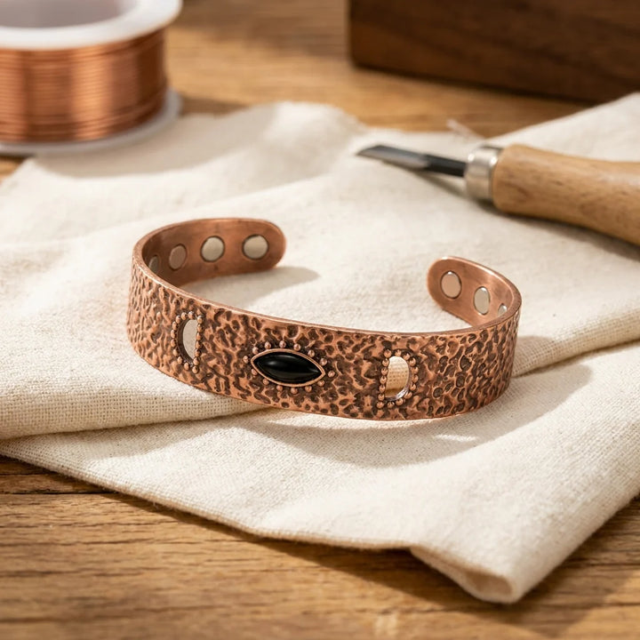 Women's copper cuff bracelet with hammered texture and central onyx stone on linen cloth