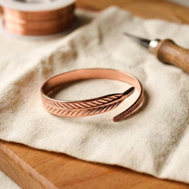 Women's copper feather bracelet with hand-engraved detailing on natural linen background