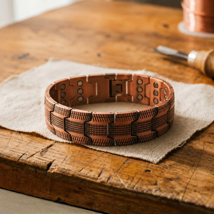 Women's copper link bracelet with textured crosshatch panels and oxidised finish on wooden surface