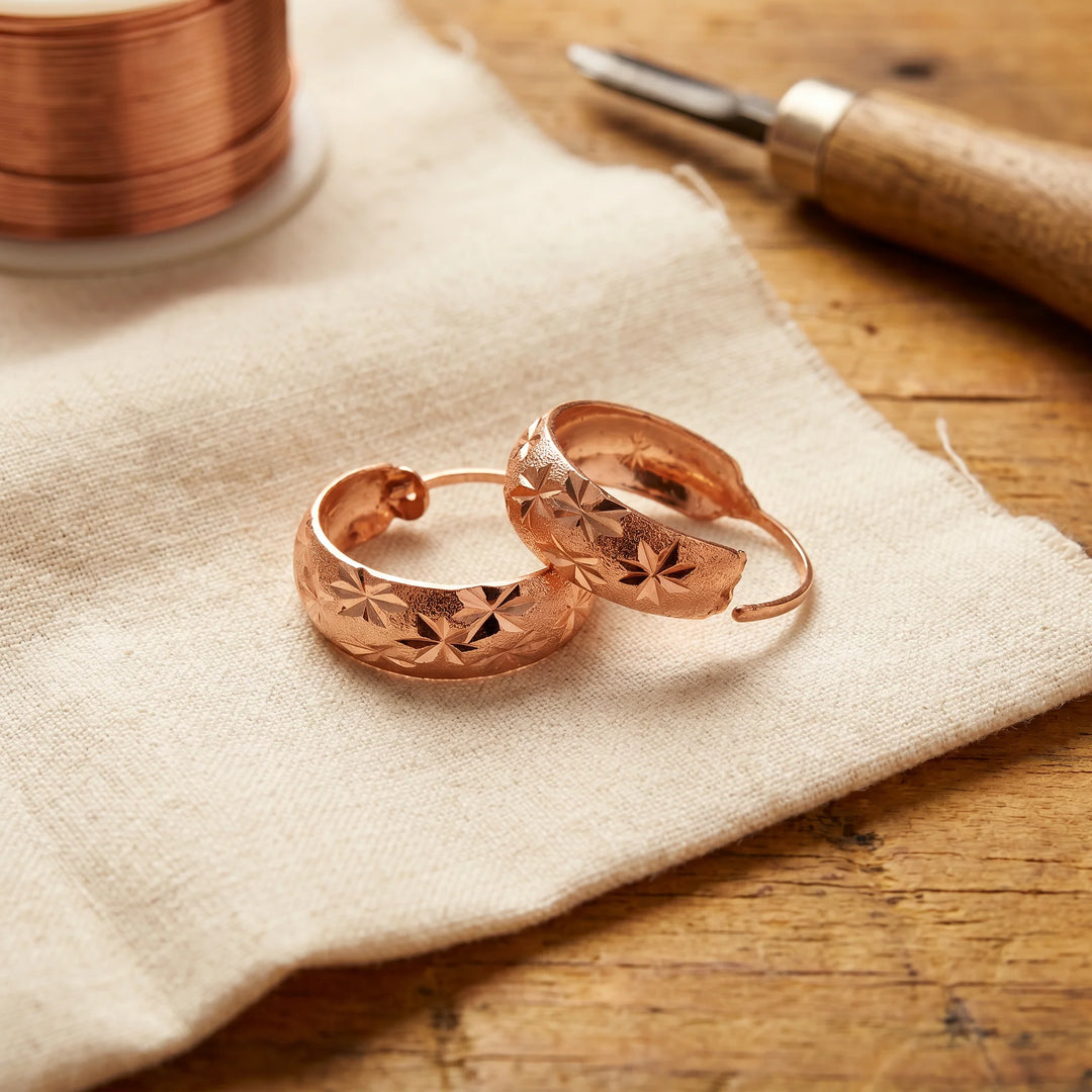 Star engraved hoop earrings with warm copper finish and hand-cut detailing displayed on linen