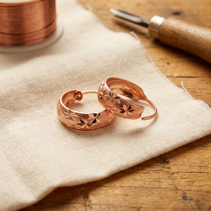 Star engraved hoop earrings with warm copper finish and hand-cut detailing displayed on linen