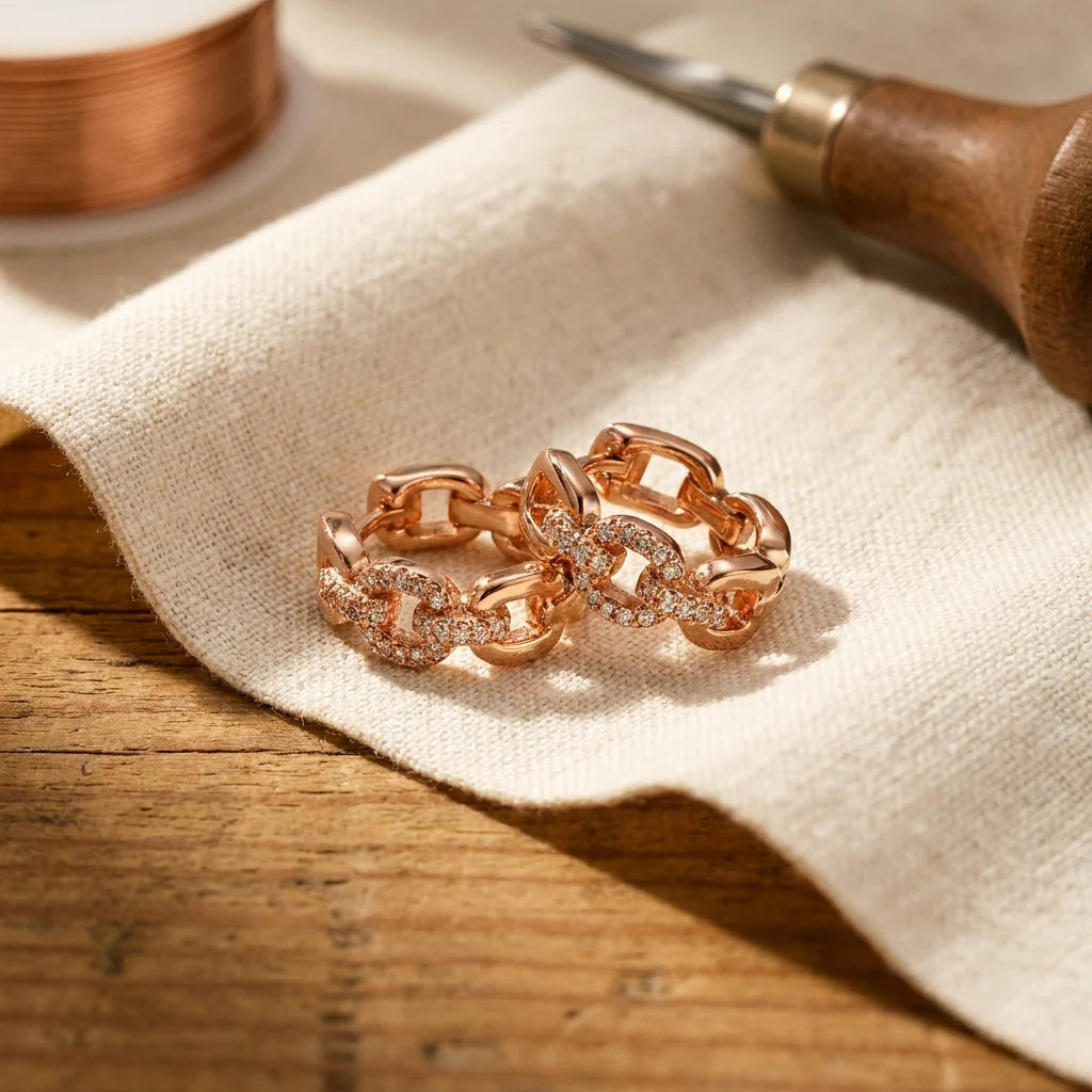 Women's rose gold-tone chain link hoop earrings with crystal embellishments displayed on neutral linen fabric