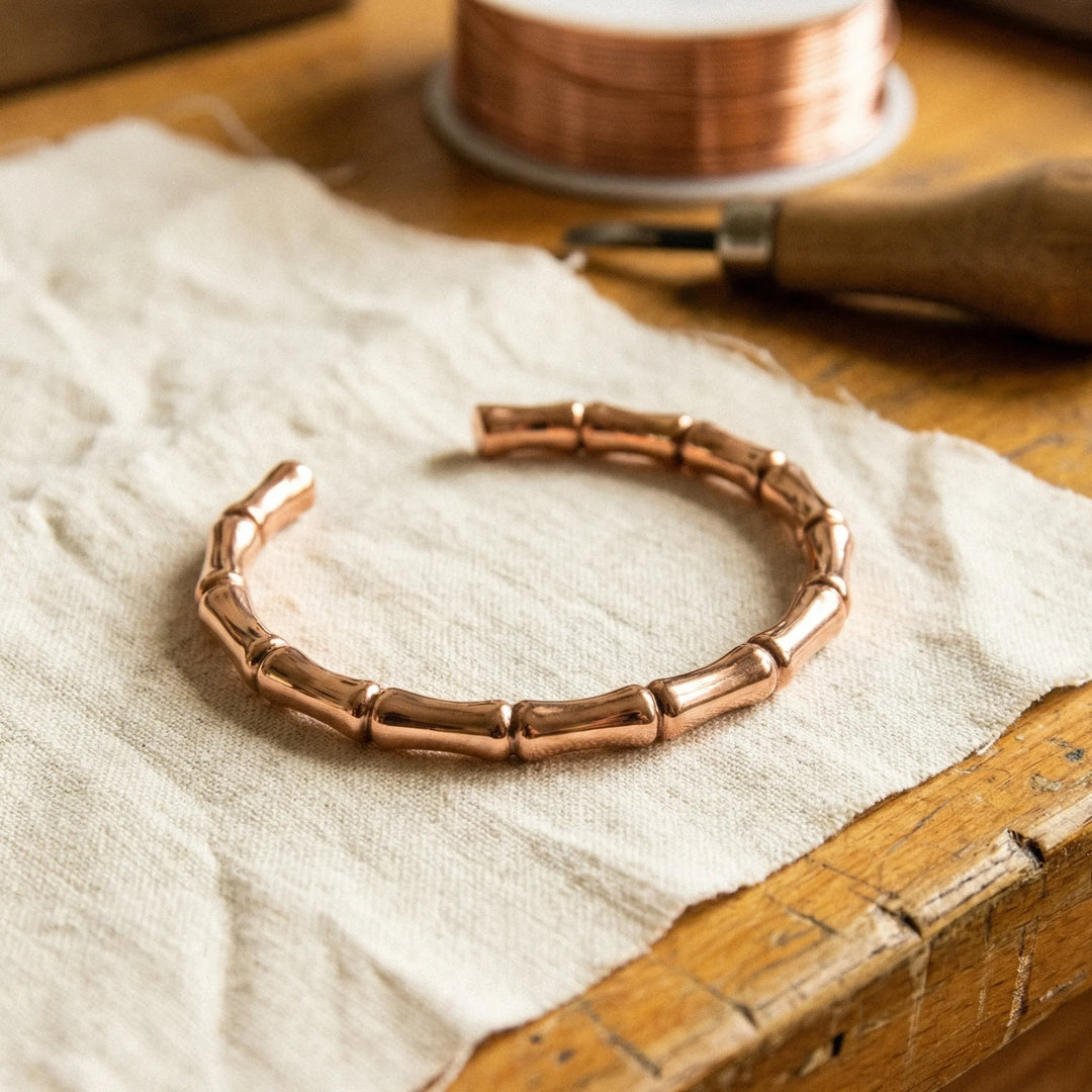 Copper bamboo bracelet with segmented design resting on linen fabric beside wooden box
