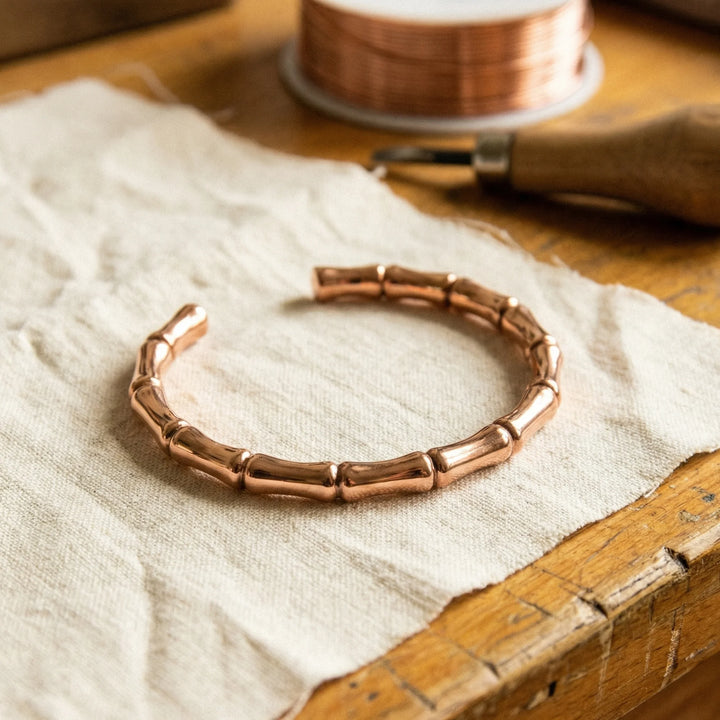 Copper bamboo bracelet with segmented design resting on linen fabric beside wooden box