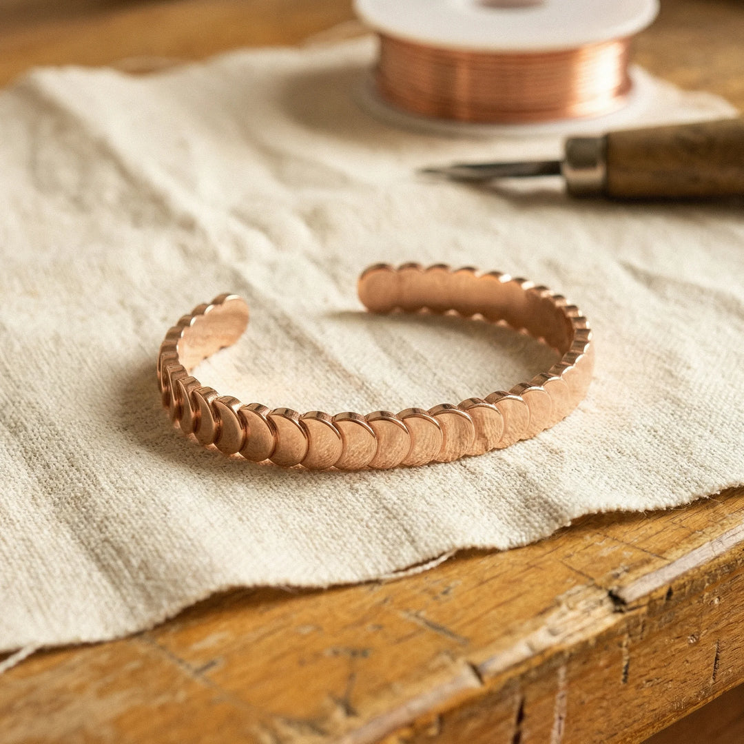 Women's copper cuff bracelet with overlapping scale design resting on linen fabric beside copper wire spool