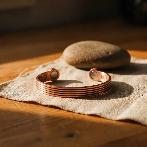 Women's copper cuff bracelet with ridged detailing resting on natural linen fabric beside stone