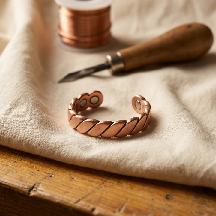 Copper twist ring with rope-style band and magnetic therapy elements resting on linen fabric beside crafting tools